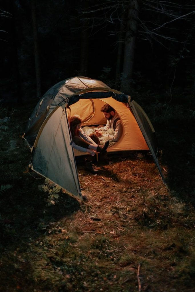 A couple enjoying a cozy evening inside a tent in the forest, illuminated warmly.